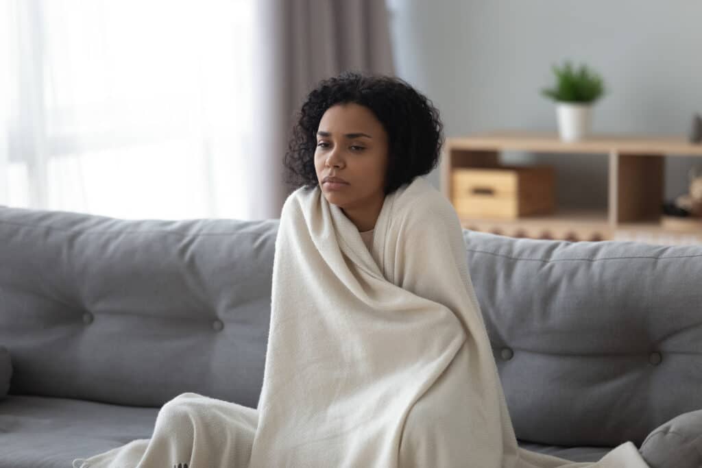 Cold feeling woman sitting on the couch wrapped in a blanket